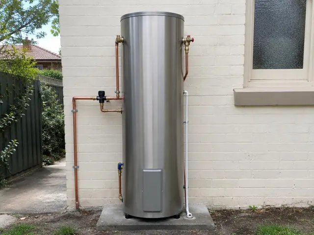 Outdoor hot water cylinder on a concrete slab beside a painted brick wall with copper pipework in Artarmon