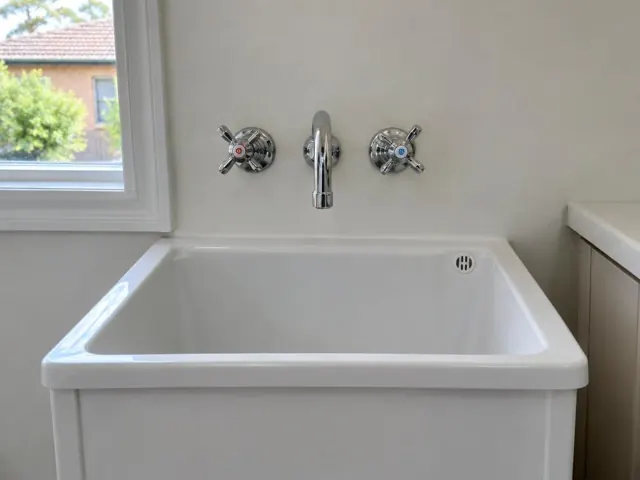 Wall-mounted tap above a white laundry tub and bench beside a window in Lane Cove